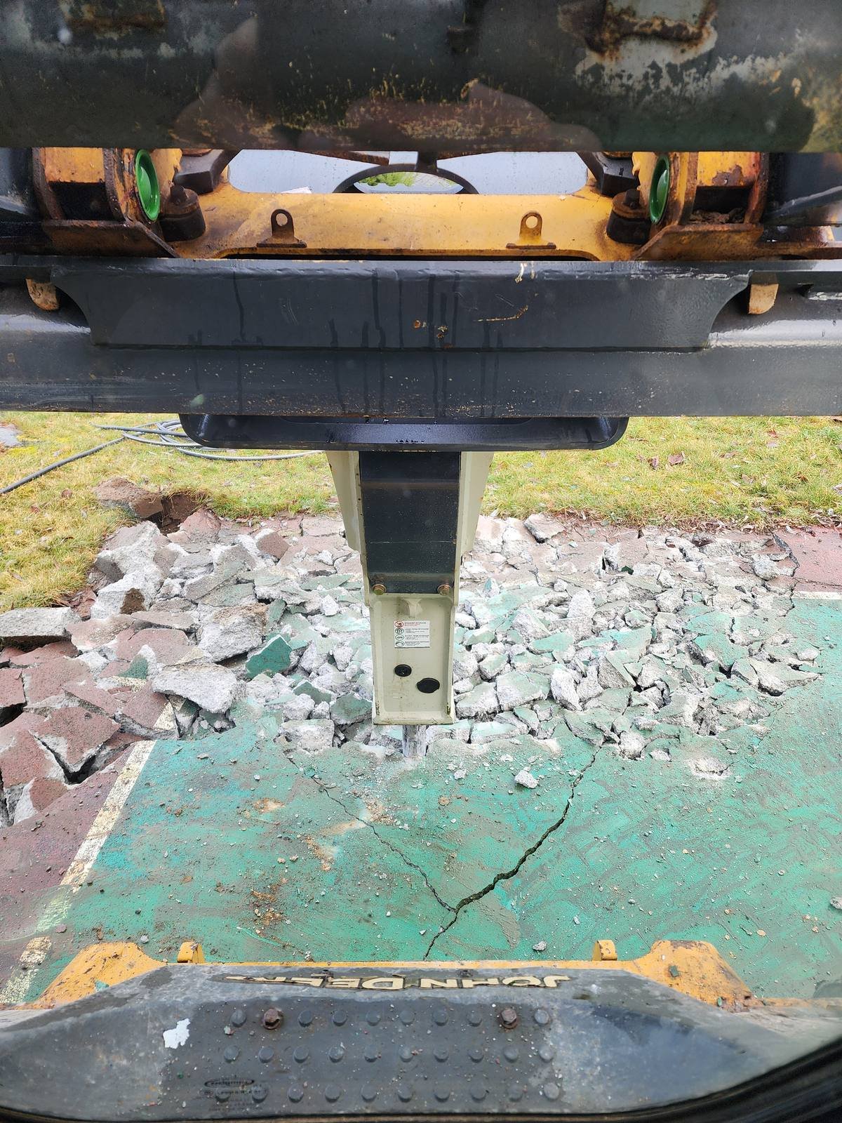 Hydraulic breaker breaking up a painted concrete slab, seen from the machine cab