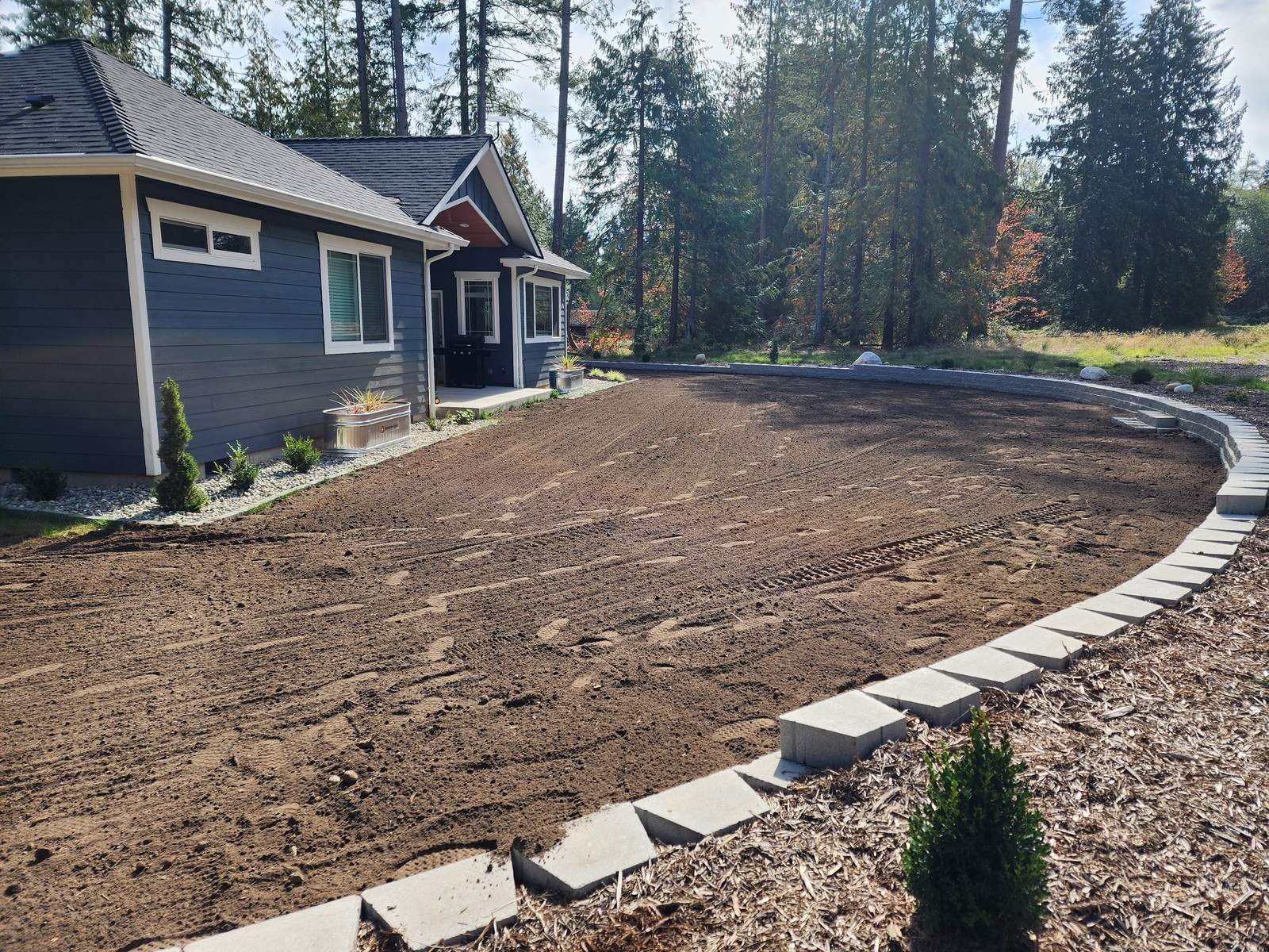 Finish-graded topsoil area bordered by concrete landscape curbing next to a house