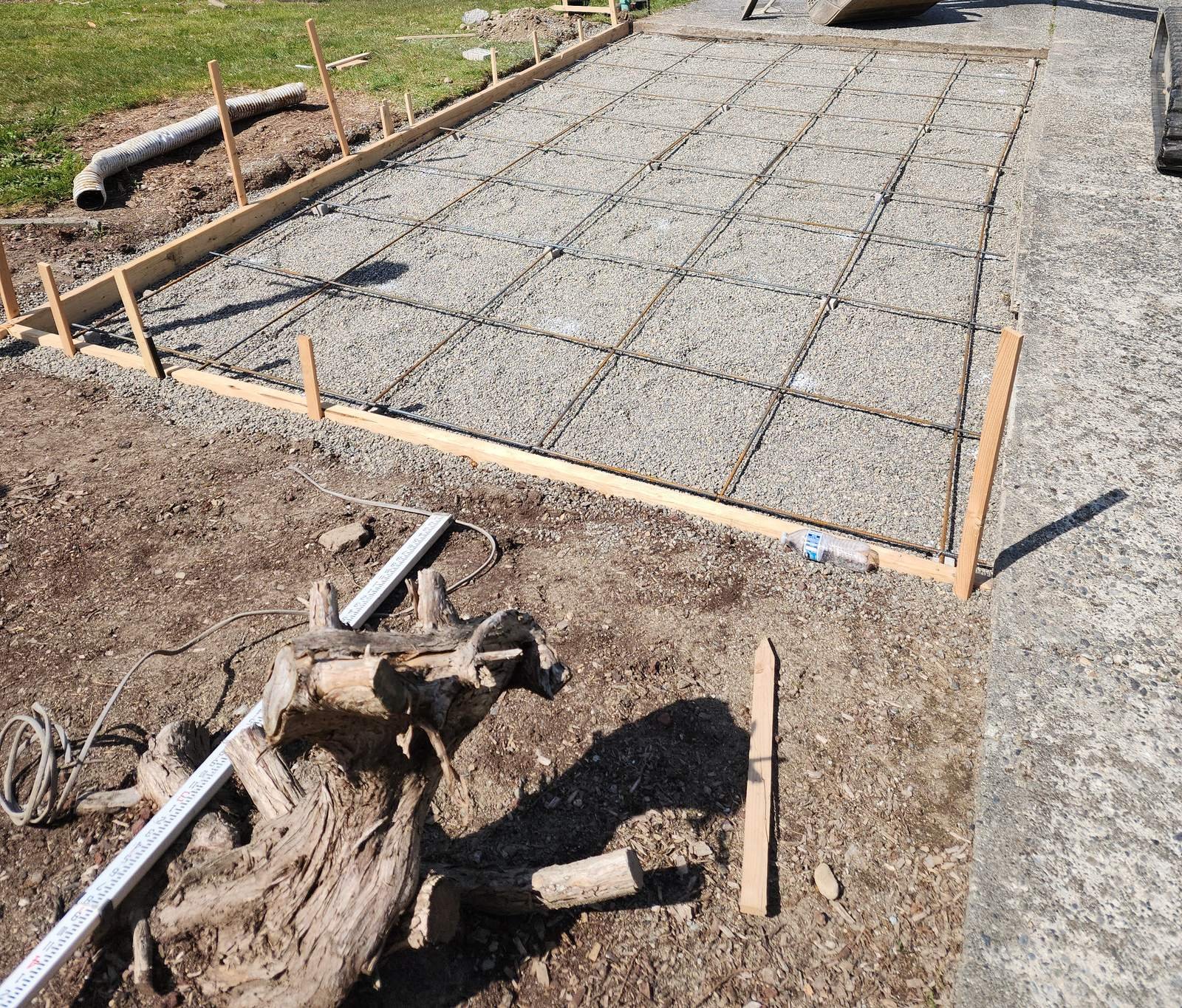 Wood forms and rebar grid set on prepared gravel base next to a driveway