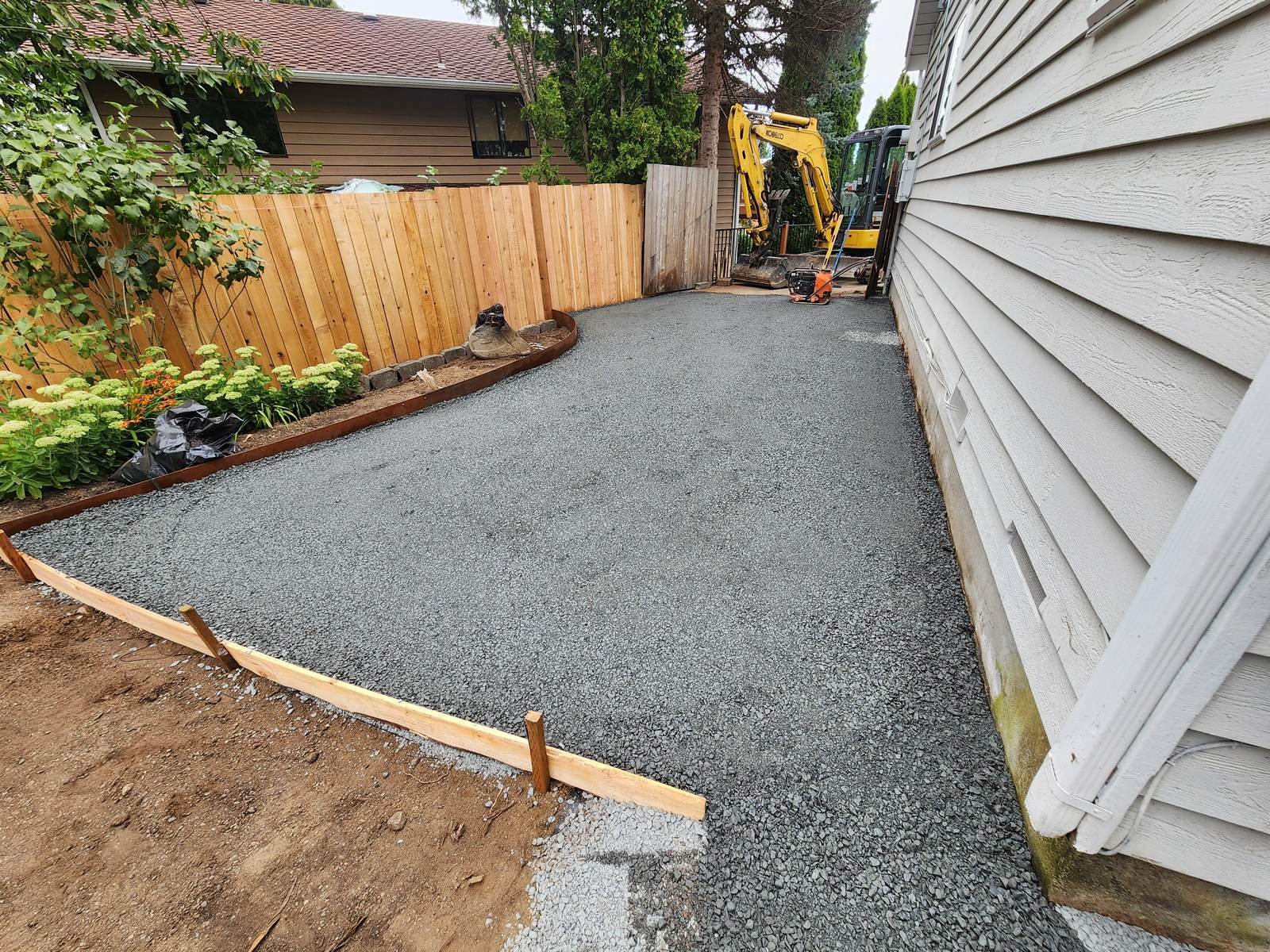 Compacted gravel subgrade with wood edge forms beside a house, ready for pavers
